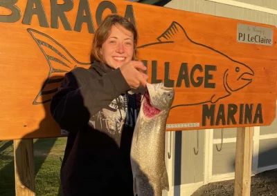 Picture of lady holding large fish in front of Baraga Village Marina sign. Keweenaw Bay, Lake Superior.